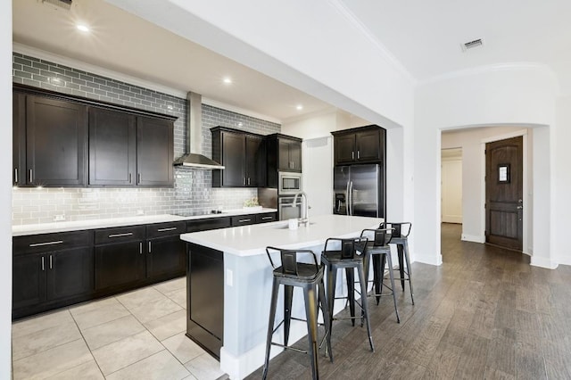 kitchen with stainless steel appliances, wall chimney range hood, a sink, crown molding, and a breakfast bar area