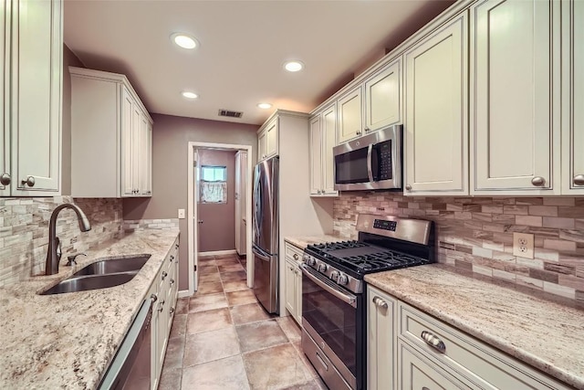 kitchen featuring appliances with stainless steel finishes, a sink, baseboards, light stone countertops, and recessed lighting