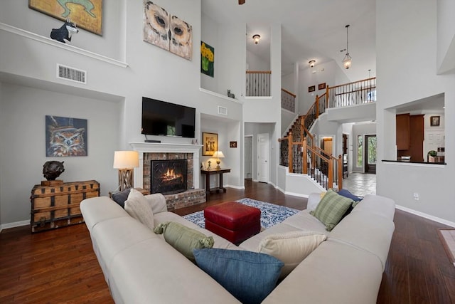 living area featuring a towering ceiling, stairway, baseboards, wood finished floors, and a brick fireplace