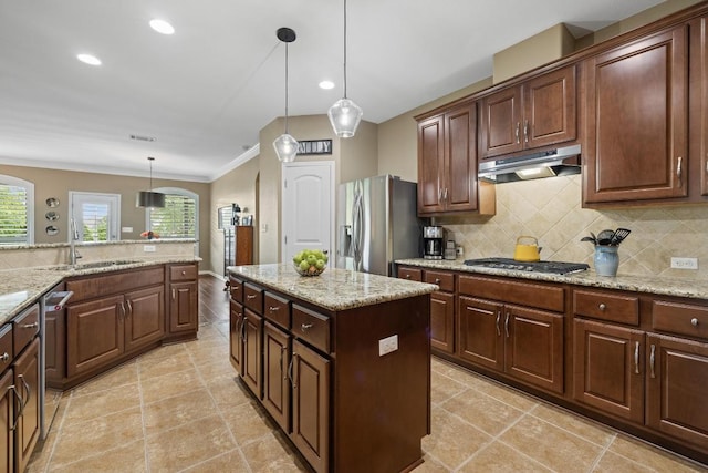 313 Monahans Dr, Georgetown, TX 78628 - kitchen with under cabinet range hood, appliances with stainless steel finishes, backsplash, decorative light fixtures, and light stone countertops