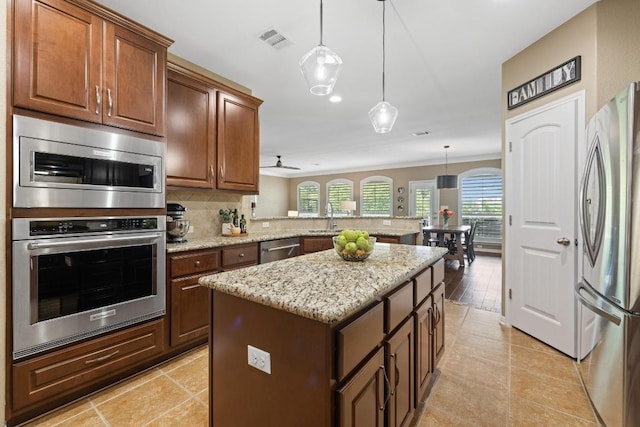 313 Monahans Dr, Georgetown, TX 78628 - kitchen featuring appliances with stainless steel finishes, a peninsula, tasteful backsplash, a center island, and light stone countertops