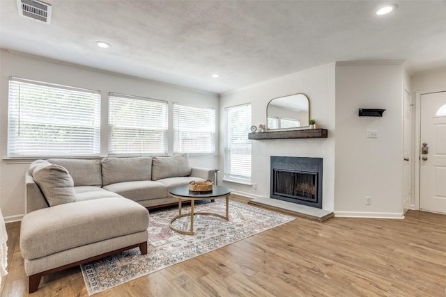 living area with baseboards, a fireplace with raised hearth, wood finished floors, recessed lighting, and crown molding