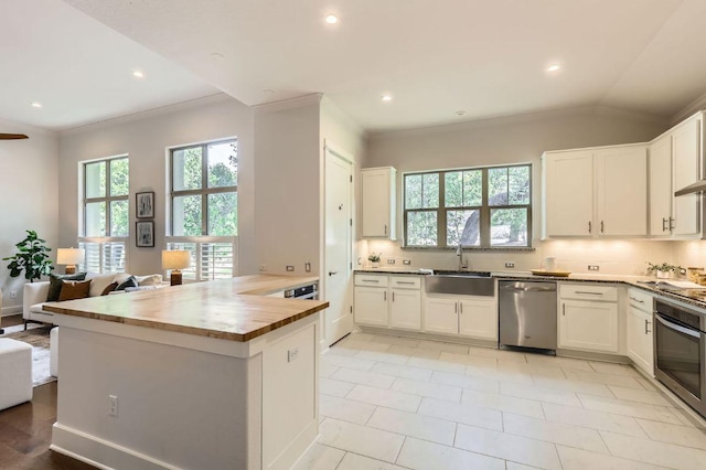 kitchen with stainless steel appliances, a sink, wooden counters, a peninsula, and white cabinets