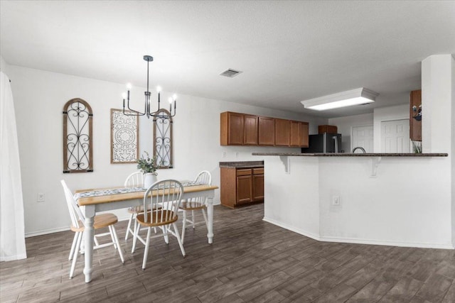 6820 Derby Downs Dr, Austin, TX 78747 - kitchen featuring freestanding refrigerator, a chandelier, brown cabinetry, a breakfast bar area, and dark wood-style flooring