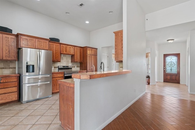 920 Barton Creek Dr, Dripping Springs, TX 78620 - kitchen featuring appliances with stainless steel finishes, a towering ceiling, tasteful backsplash, brown cabinetry, and baseboards