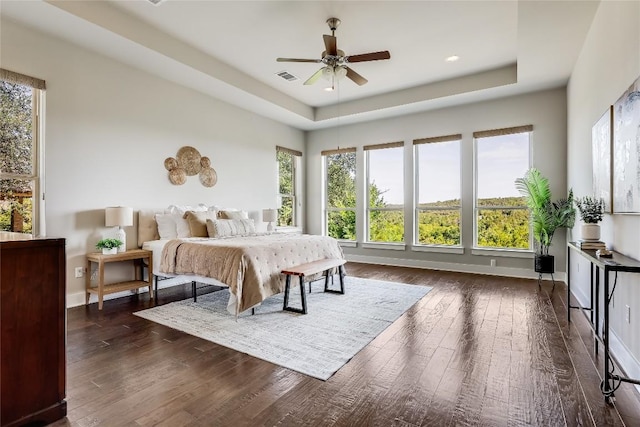 bedroom with wood finished floors, multiple windows, a tray ceiling, and baseboards
