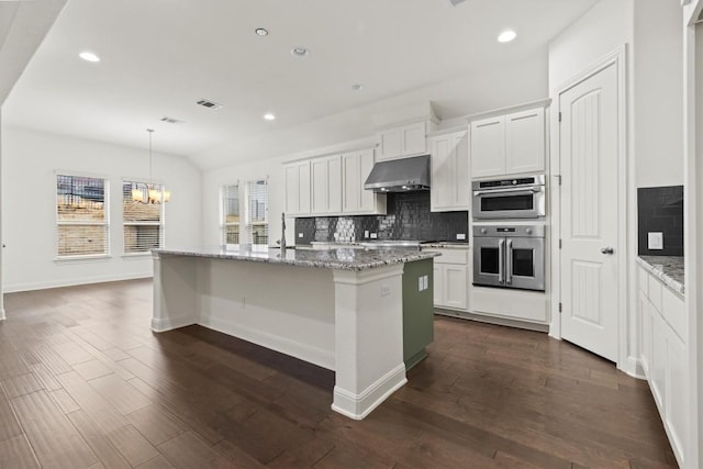 kitchen featuring decorative backsplash, a chandelier, an island with sink, under cabinet range hood, and dark wood finished floors