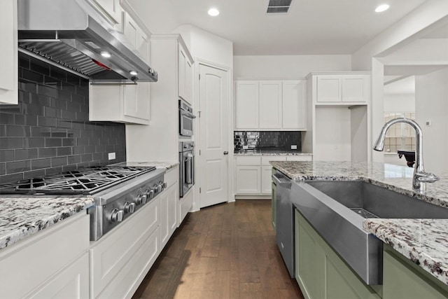 kitchen featuring wall chimney range hood, stainless steel appliances, a sink, tasteful backsplash, and white cabinetry