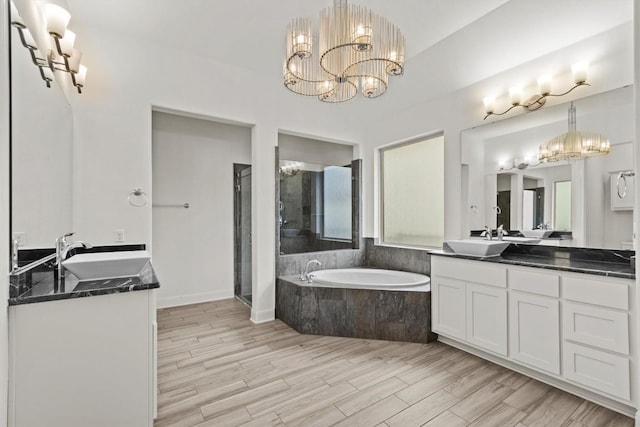 full bath with a chandelier, a stall shower, a bath, two vanities, and wood finished floors