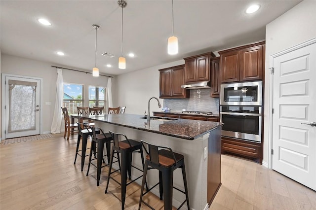 8716 Mina Dr, Austin, TX 78747 - kitchen with stainless steel appliances, a sink, under cabinet range hood, backsplash, and a breakfast bar area