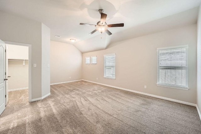 unfurnished bedroom with light carpet, baseboards, a spacious closet, vaulted ceiling, and a ceiling fan