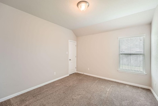 empty room featuring carpet floors, vaulted ceiling, and baseboards