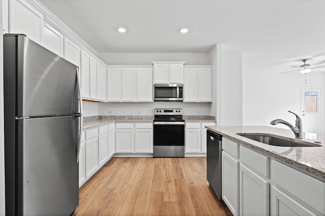 kitchen featuring stainless steel appliances, a sink, white cabinets, recessed lighting, and light wood-style floors
