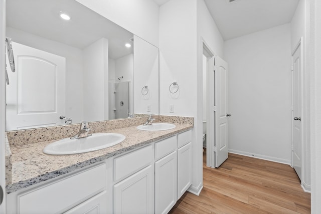 bathroom with toilet, wood finished floors, a shower, double vanity, and recessed lighting