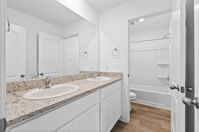 bathroom with toilet, wood finished floors, double vanity, and shower / bath combination