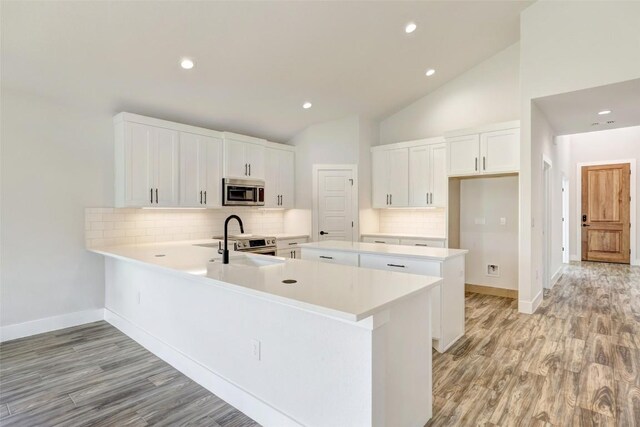 9601 Eloquence Dr, Manor, TX 78653 - kitchen with appliances with stainless steel finishes, tasteful backsplash, a peninsula, vaulted ceiling, and light wood finished floors