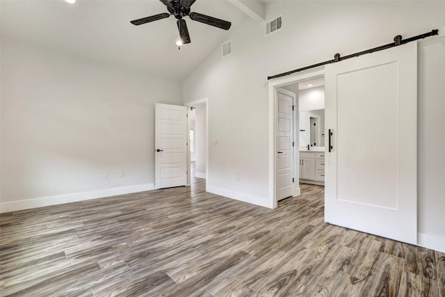 9601 Eloquence Dr, Manor, TX 78653 - unfurnished bedroom with a barn door, high vaulted ceiling, wood finished floors, beamed ceiling, and connected bathroom