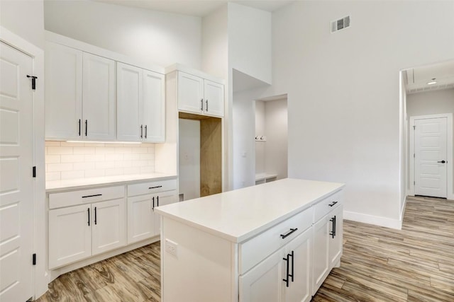 9601 Eloquence Dr, Manor, TX 78653 - kitchen featuring light wood finished floors, tasteful backsplash, white cabinets, a towering ceiling, and light countertops