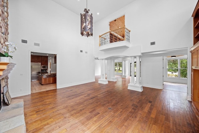 106 Sendera Bonita, Austin, TX 78734 - unfurnished living room featuring ornate columns, a high ceiling, hardwood / wood-style flooring, a stone fireplace, and a chandelier