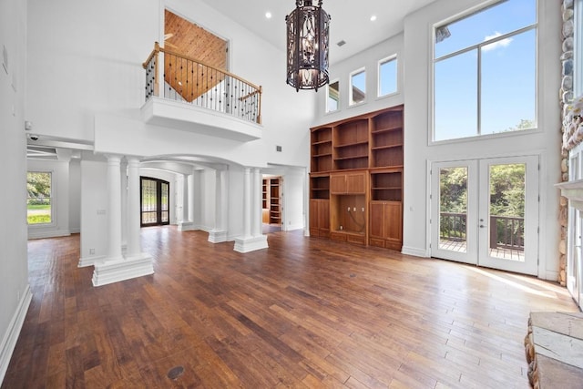 106 Sendera Bonita, Austin, TX 78734 - unfurnished living room featuring ornate columns, a towering ceiling, hardwood / wood-style floors, french doors, and arched walkways