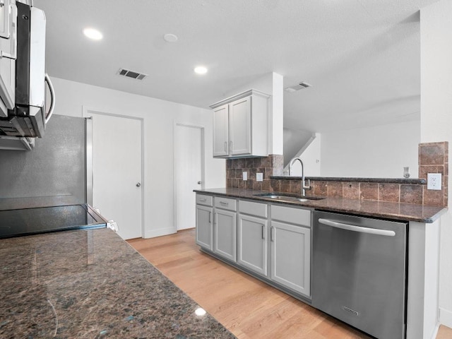109 Orange Tree Ln, Georgetown, TX 78626 - kitchen featuring stainless steel appliances, a sink, light wood-style floors, backsplash, and dark stone counters