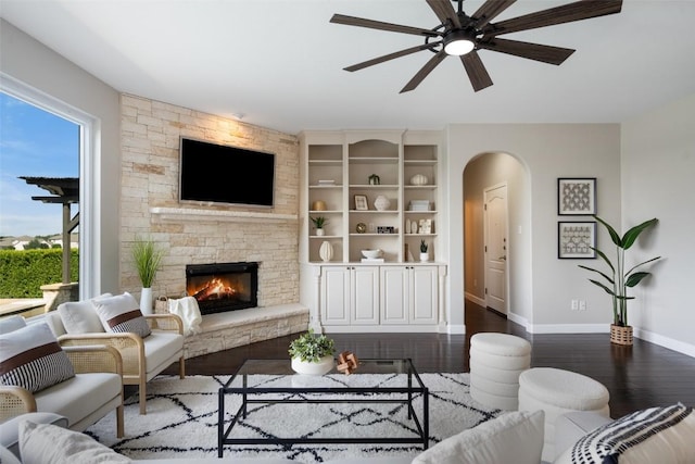 living room featuring healthy amount of natural light, arched walkways, dark wood finished floors, and baseboards