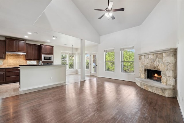 21816 Agarito Ln, Spicewood, TX 78669 - unfurnished living room with high vaulted ceiling, a ceiling fan, wood finished floors, a stone fireplace, and baseboards