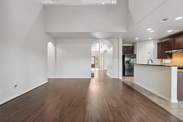 21816 Agarito Ln, Spicewood, TX 78669 - kitchen with stainless steel fridge with ice dispenser, arched walkways, open floor plan, a towering ceiling, and dark brown cabinets