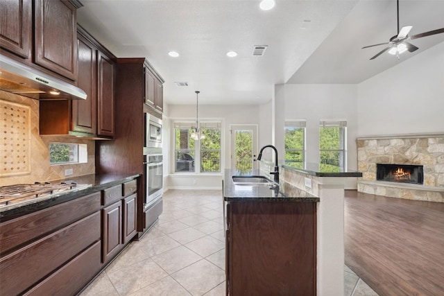 21816 Agarito Ln, Spicewood, TX 78669 - kitchen featuring appliances with stainless steel finishes, a sink, a stone fireplace, under cabinet range hood, and dark stone counters