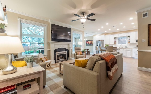 living area with crown molding, a ceiling fan, a fireplace, light wood-type flooring, and baseboards