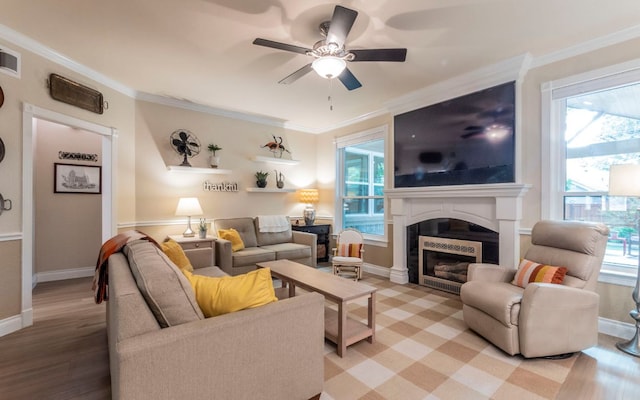 living room with ceiling fan, healthy amount of natural light, a fireplace, crown molding, and light wood-type flooring