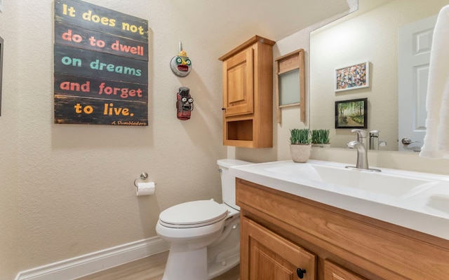 bathroom featuring toilet, vanity, wood finished floors, and baseboards