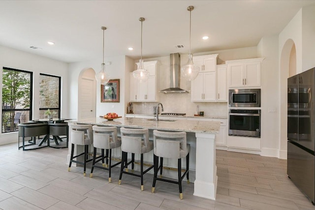 604 Rawson Bnd, Austin, TX 78738 - kitchen featuring stainless steel appliances, wall chimney range hood, backsplash, white cabinetry, and a kitchen island with sink