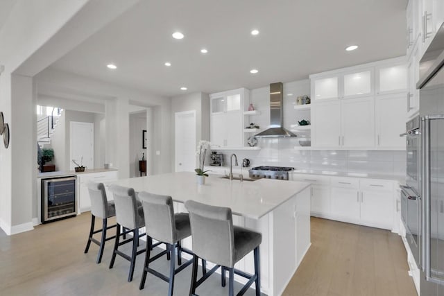 kitchen featuring wine cooler, wall chimney exhaust hood, a sink, open shelves, and light countertops