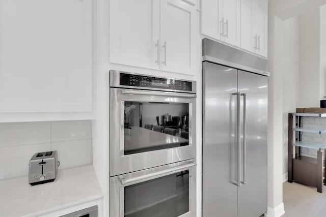kitchen featuring appliances with stainless steel finishes, white cabinetry, decorative backsplash, and light stone counters