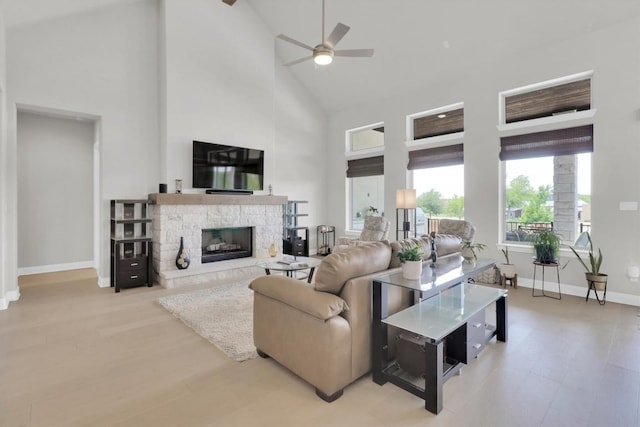 living area with high vaulted ceiling, a ceiling fan, a stone fireplace, baseboards, and wood finished floors