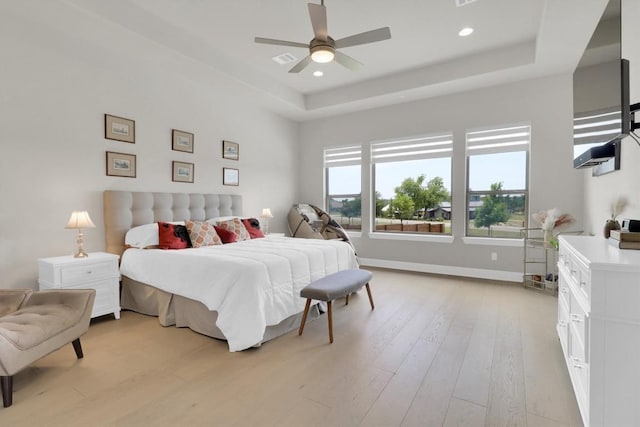 bedroom with light wood finished floors, a tray ceiling, baseboards, recessed lighting, and ceiling fan