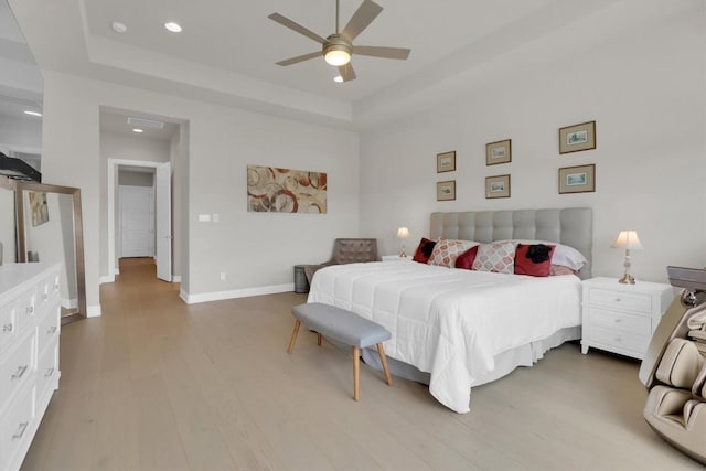 bedroom featuring a tray ceiling, light wood finished floors, recessed lighting, baseboards, and a ceiling fan