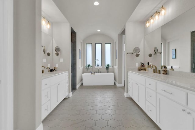 bathroom with two vanities, a freestanding tub, recessed lighting, and baseboards