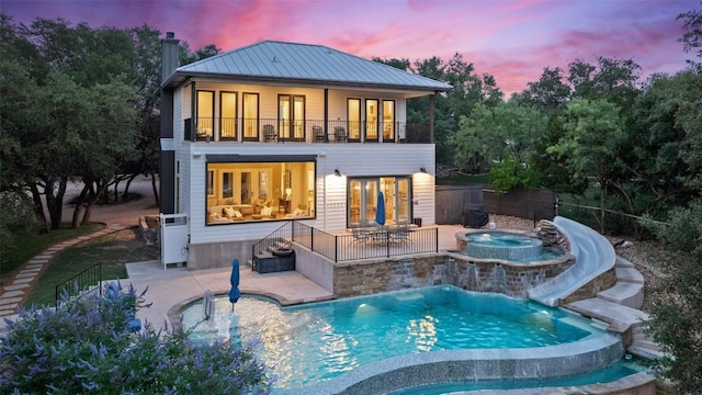 1348 Lake Shore Dr, Spicewood, TX 78669 - back of house at dusk featuring an in-ground hot tub, a balcony, a chimney, and a patio area
