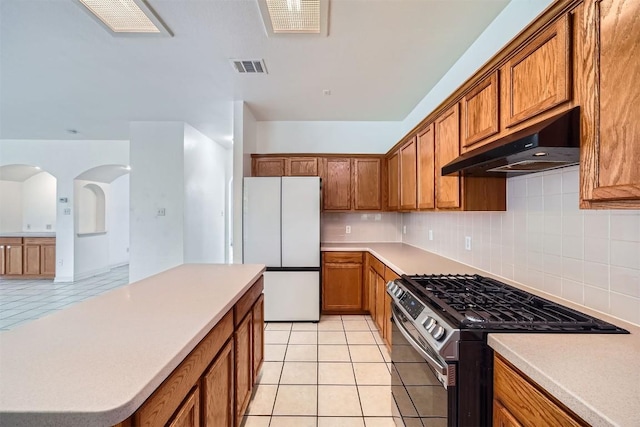 4712 Ramies Run, Austin, TX 78749 - kitchen with stainless steel gas range oven, under cabinet range hood, freestanding refrigerator, brown cabinets, and light tile patterned floors