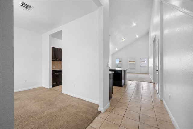 hallway featuring light carpet, lofted ceiling, baseboards, arched walkways, and light tile patterned floors