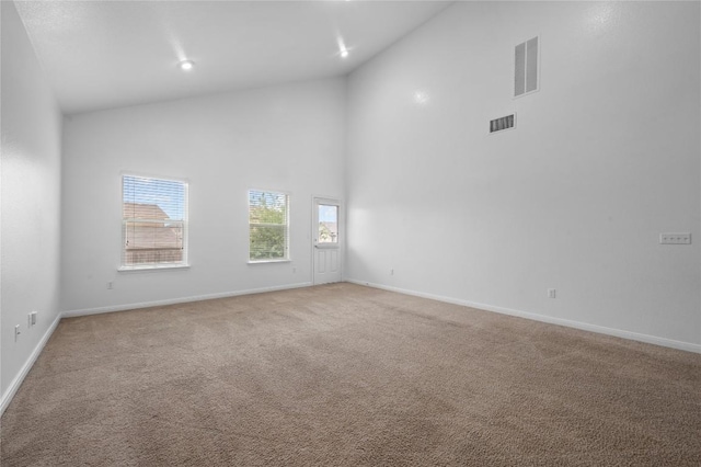 carpeted spare room featuring high vaulted ceiling and baseboards