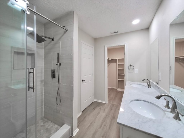 9512 Meadowheath Dr, Austin, TX 78729 - bathroom featuring a stall shower, a textured ceiling, wood finished floors, baseboards, and double vanity