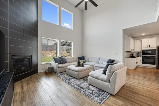 707 Sugar Cane Rd, Buda, TX 78610 - living room with a towering ceiling, ceiling fan, light wood-type flooring, a tile fireplace, and baseboards