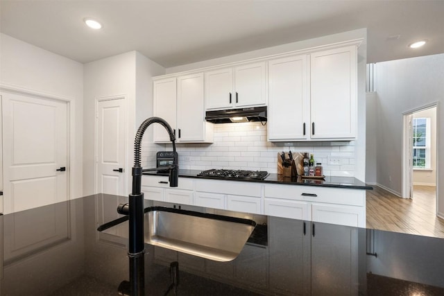 707 Sugar Cane Rd, Buda, TX 78610 - kitchen with under cabinet range hood, a sink, dark countertops, white cabinetry, and recessed lighting