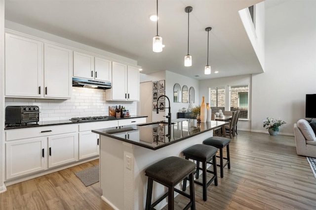 707 Sugar Cane Rd, Buda, TX 78610 - kitchen with a sink, under cabinet range hood, dark countertops, light wood-style flooring, and gas stovetop