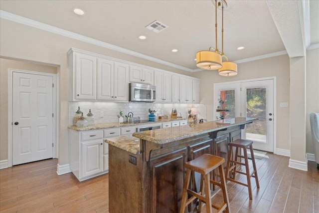 1409 Old Mill Rd, Salado, TX 76571 - kitchen featuring stainless steel microwave, white cabinets, a kitchen bar, light wood-type flooring, and crown molding