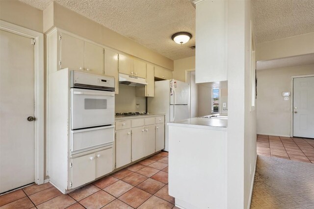 105 E St Johns Ave, Austin, TX 78752 - kitchen with a warming drawer, white appliances, under cabinet range hood, a textured ceiling, and light tile patterned flooring