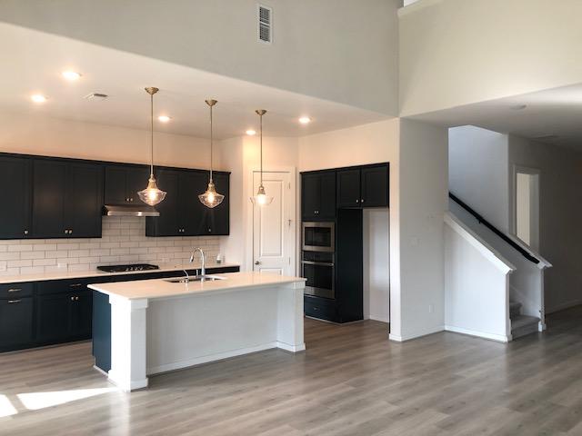 22617 Agave Grove Dr, Lago Vista, TX 78645 - kitchen with under cabinet range hood, cooktop, stainless steel microwave, dark cabinets, and light wood-style floors